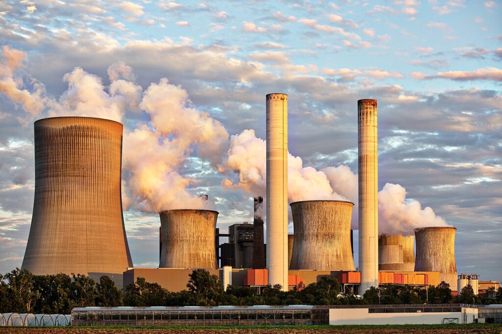 power Generation plant emitting steam and surrounded by electrical transmission lines.